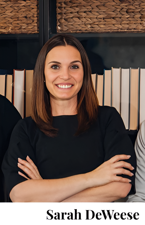 Smiling woman with crossed arms standing in front of bookshelves.